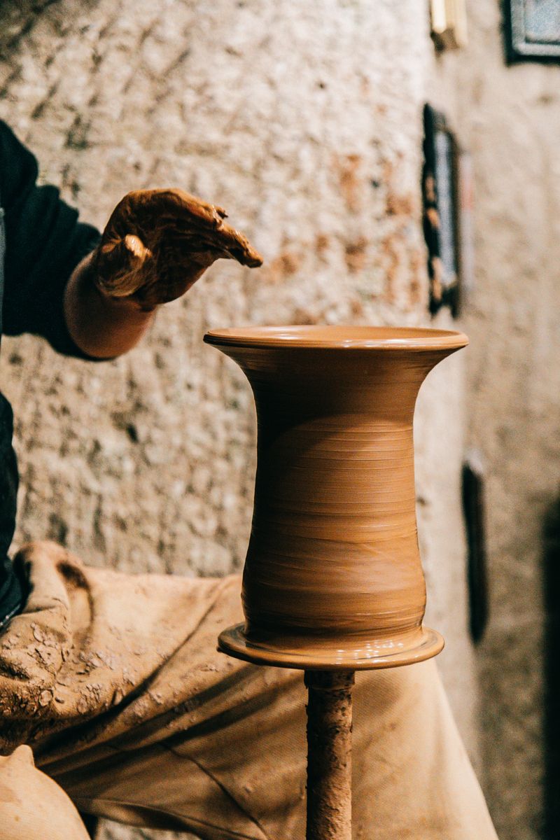 Crop anonymous male shaping brown pot on pottery wheel in daytime on blurred background