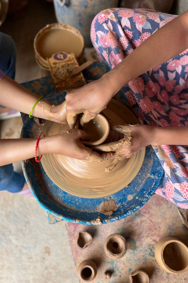 Pottery making with hands shaping clay on a wheel, teamwork in artistic creation.
