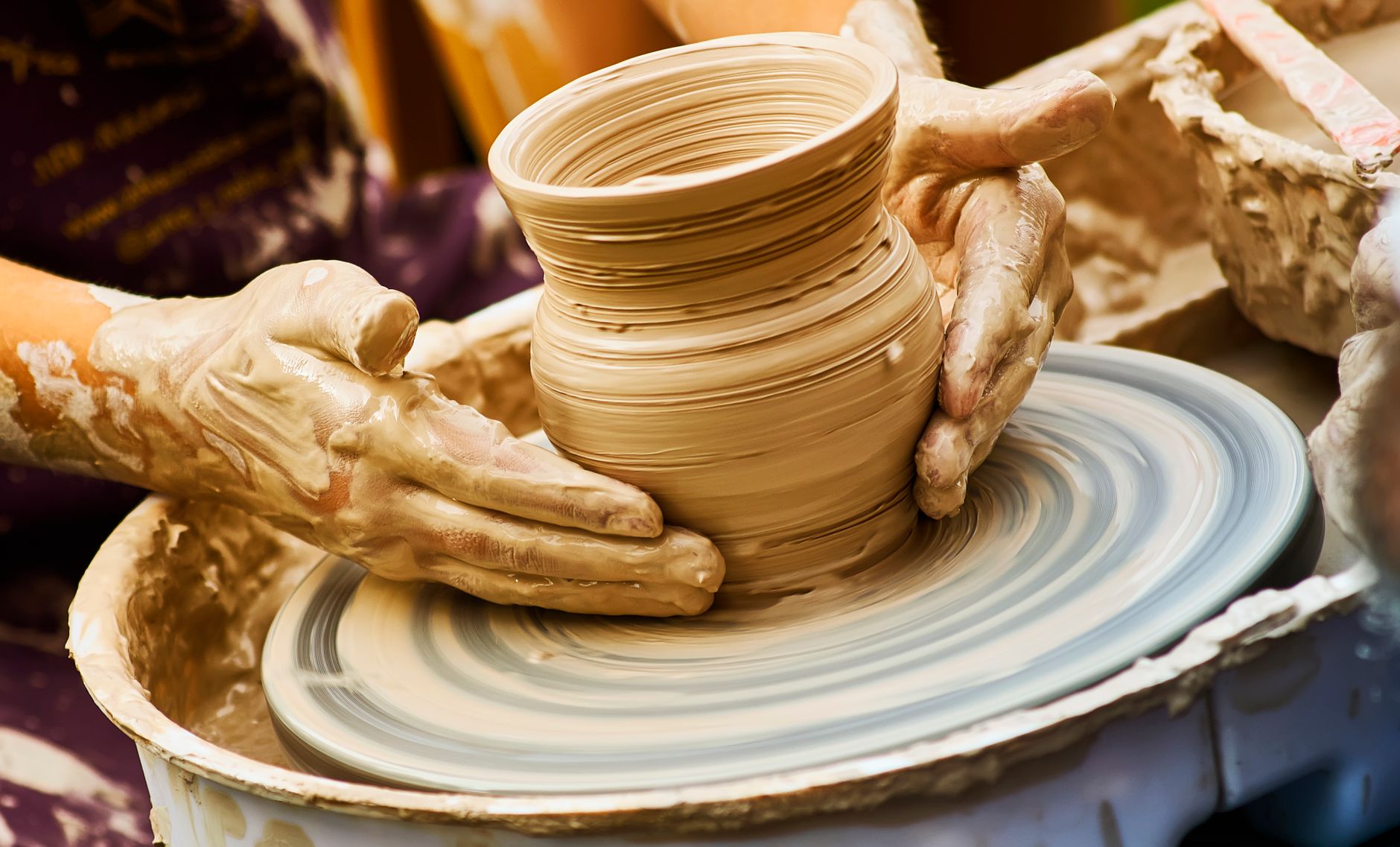 Hands shaping a clay pot on a spinning pottery wheel, showcasing artisanal craftsmanship.